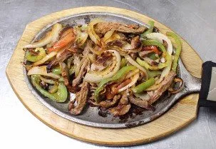 Sizzling skillet of fajitas with grilled peppers, onions and tomatoes